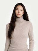 Woman wearing a beige turtleneck sweater against a white background