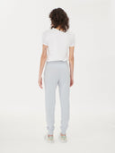 back view of a woman wearing a white t-shirt and light gray sweatpants on a white background. #color_ice-blue