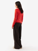 back view of a woman wearing a red sweater and black pants on a white background. #color_red-orange