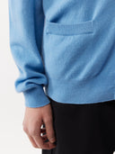 Close-up of a person wearing a light blue sweater with a pocket on a white background. #color_lichen-blue