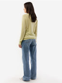 back view of a woman wearing a light green sweater and blue jeans on a white background. #color_cream-yellow
