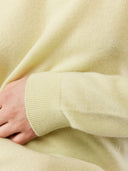 Close-up of a light yellow sweater with a hand resting on the armhole. #color_cream-yellow