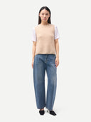 Woman wearing a beige vest over a white shirt and blue jeans on a white background #color_beige