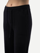 Close-up of a person wearing black knit pants with a drawstring waistband, shown against a plain light background.