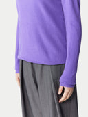 Person wearing a purple sweater and gray pants on a light gray background. #color_purple