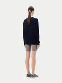 Person wearing a navy long-sleeve top and beige shorts on a white background. #color_navy-blue