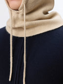 Close-up of a person wearing a beige knitted hoodie with a navy outfit underneath.
