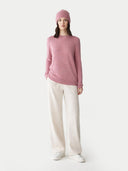 Woman wearing a pink sweater and beanie with white pants on a white background #color_lilas