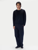 A man modeling a dark navy long-sleeve crewneck sweater and matching navy trousers against a plain light gray studio background.