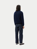 Person wearing a navy sweater and dark jeans on a white background. #color_navy-blue