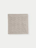 A knitted pillow cover in solid color with a cable knit pattern.