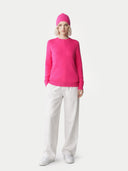 Person wearing a bright pink sweater and hat with white pants on a light gray background