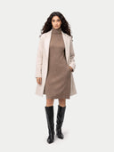 Woman wearing a beige coat over a brown dress with black knee-high boots on a white background. #color_taupe #ai-image