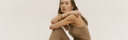 Spring–Summer 2026 collection — woman in a beige knit cashmere tank top with gold bangles, arms resting on her knee