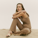 Spring–Summer 2026 collection — woman in a beige knit cashmere tank top and pants seated on sand