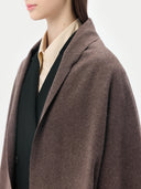 Close-up of a person wearing a brown coat over a black shirt and beige blouse on a white background