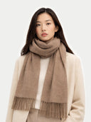 Woman wearing a beige scarf with fringe on a white background