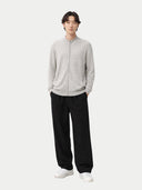 A man modeling a light gray zip-up knit sweater with a stand collar, paired with black wide-leg trousers and white sneakers, against a solid light gray background. #color_steel-silver #ai-image