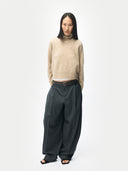 Person wearing a beige sweater and dark gray wide-leg pants on a white background