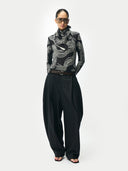 Person wearing a black and white patterned top with high-waisted black pants on a white background