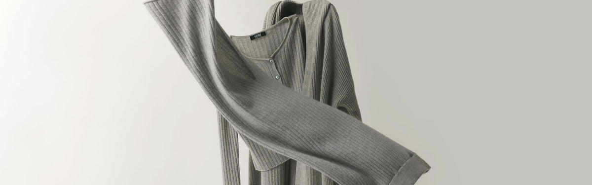 Grey ribbed cashmere cardigan caught mid-swing against a pale grey wall