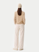 Person wearing a beige sweater and white pants on a white background