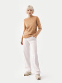 Person wearing a beige sweater and white pants on a white background. #color_light-brown