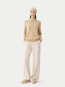 Person wearing a beige sweater and white pants on a white background #color_beige