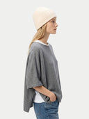 Woman wearing a gray poncho, white beanie, and blue jeans on a light background. #color_off-white #ai-image