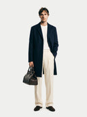 Man wearing a navy coat, white shirt, beige pants, and holding a brown leather bag on a white background. #color_navy #ai-image