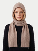 A model wearing a ribbed knit hooded beanie and a matching long scarf in a light taupe-beige color, paired with a black cable-knit sweater against a plain light gray background.#color_beige