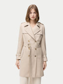 A woman wearing a beige double-breasted cashmere trench coat with a belt and lapel neckline. #color_warm-grey