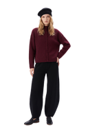 Woman in a wine red braided-cable high-neck cashmere jumper, black barrel-leg knit trousers, a black knit beret and black loafers