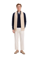 Man in a navy half-zip cashmere jumper with a beige fringed cashmere scarf, off-white trousers and golden brown loafers