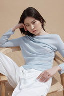 A woman in a pale blue lightweight cashmere top seated on a wooden chair in the desert