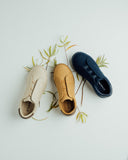Three CashmereTech sneakers in cream, tan and navy laid out with leaves