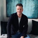 Martin Parker seated on a sofa in a navy blazer in front of a turquoise painting