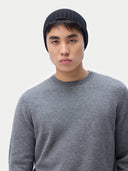 Person wearing a gray sweater and black knit beanie against a white background