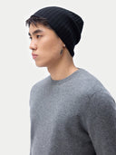 Person wearing a black knit beanie and gray sweater on a white background