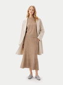 Woman wearing a beige coat, sweater, and skirt on a white background. #color_dusty-beige #ai-image