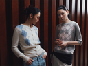 Two women in argyle cashmere knits, a cream button cardigan with jeans and a grey GOBI jumper, by wood panelling