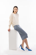 A model in a cream cashmere sweater and blue cashmere skirt seated on a white block
