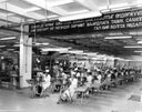 Black-and-white archive photograph of GOBI's early sewing hall, rows of workers at machines beneath a banner