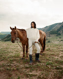 A woman in a cream cashmere sweater standing beside a horse on the Mongolian steppe