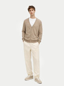 Man wearing a beige cardigan, white shirt, and cream pants on a white background