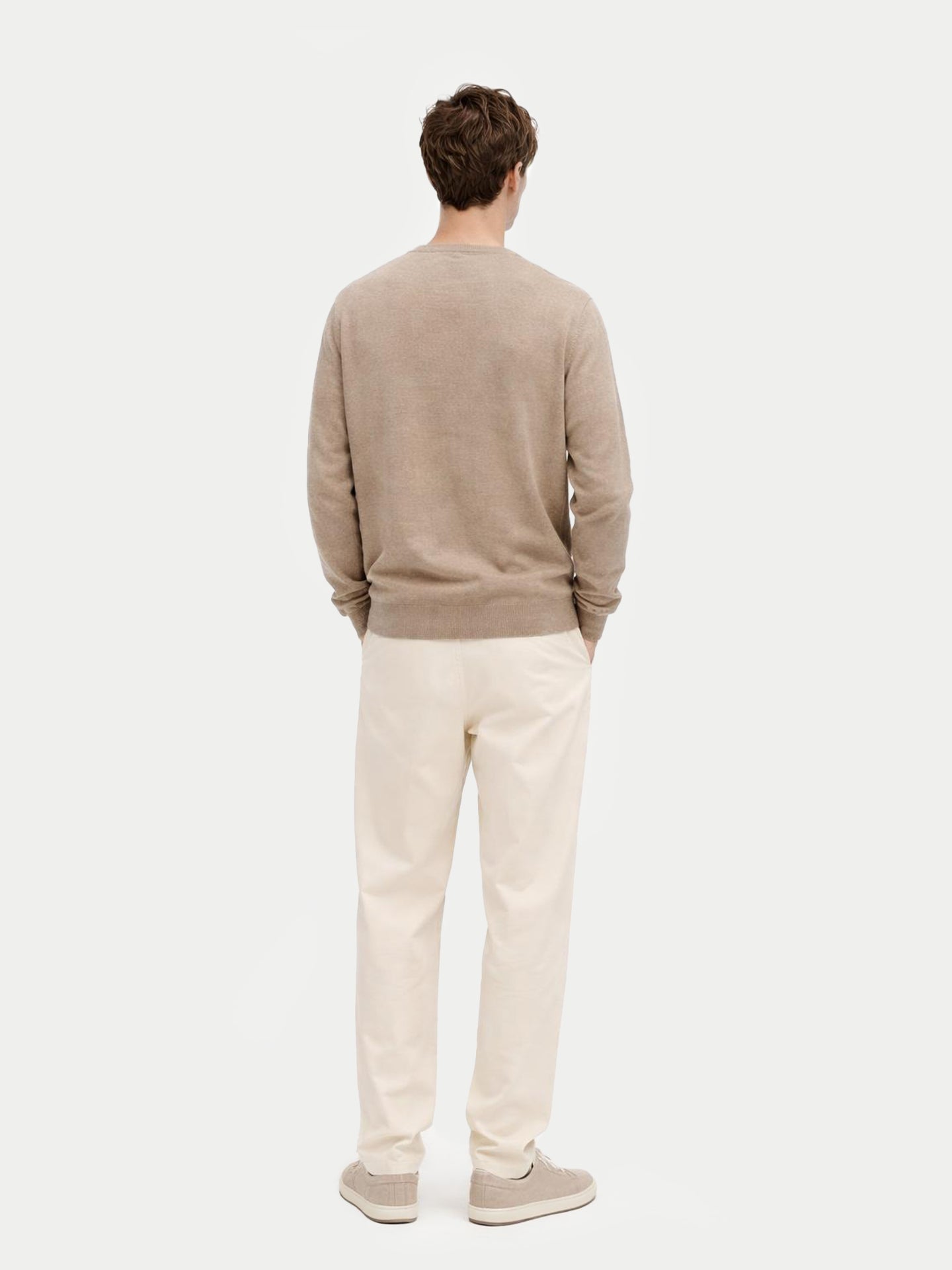 Man wearing a beige sweater and light-colored pants on a white background