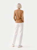back view of a woman wearing a brown sweater and white pants on a light background. #color_light-brown