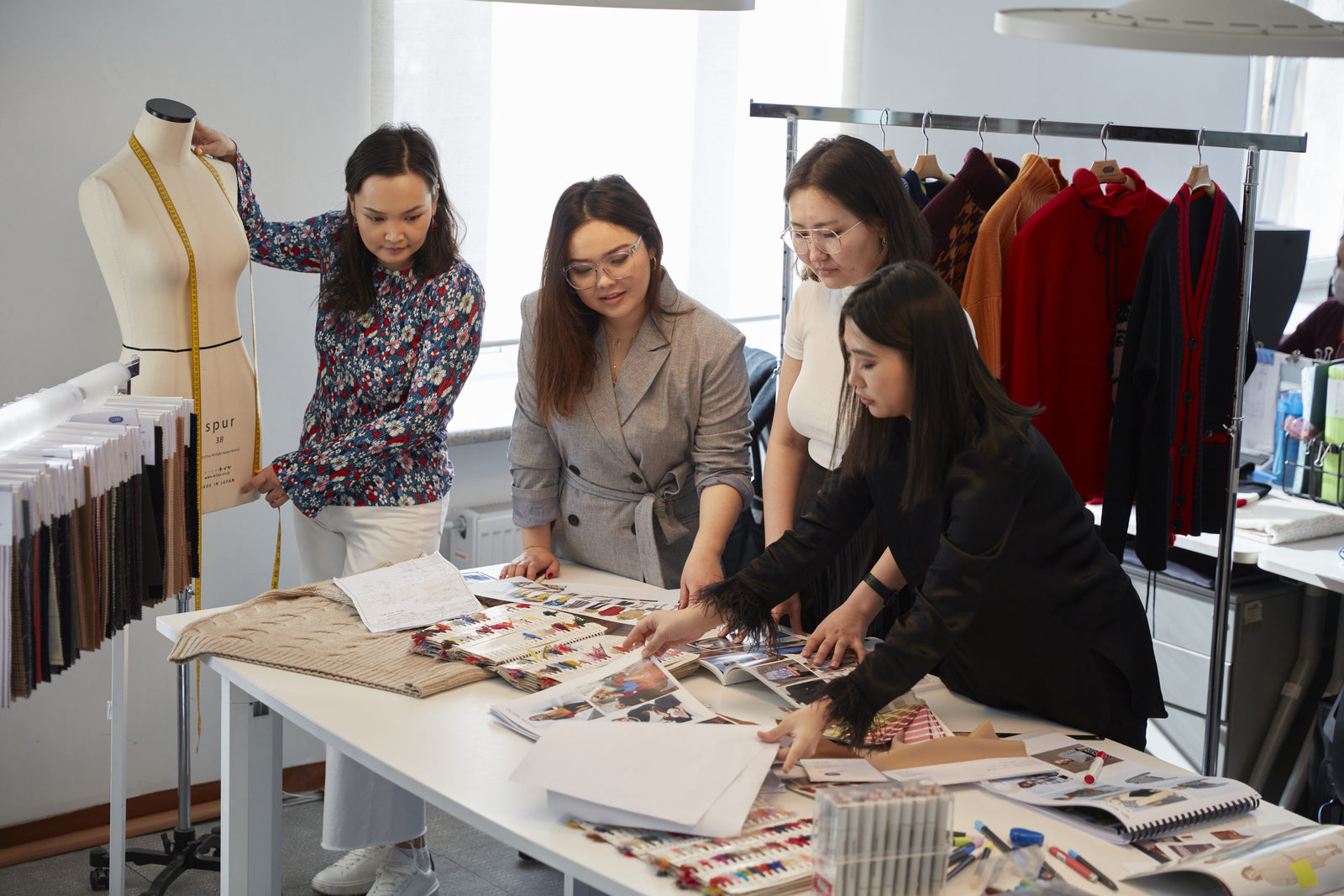 GOBI's design team around a worktable of fabric swatches and sketches beside a dress form