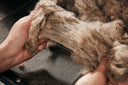 Hands lifting a handful of raw brown cashmere over a sorting mesh at GOBI's primary factory