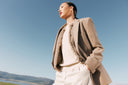A woman in a camel natural-colour cashmere coat and cream knit against a blue sky